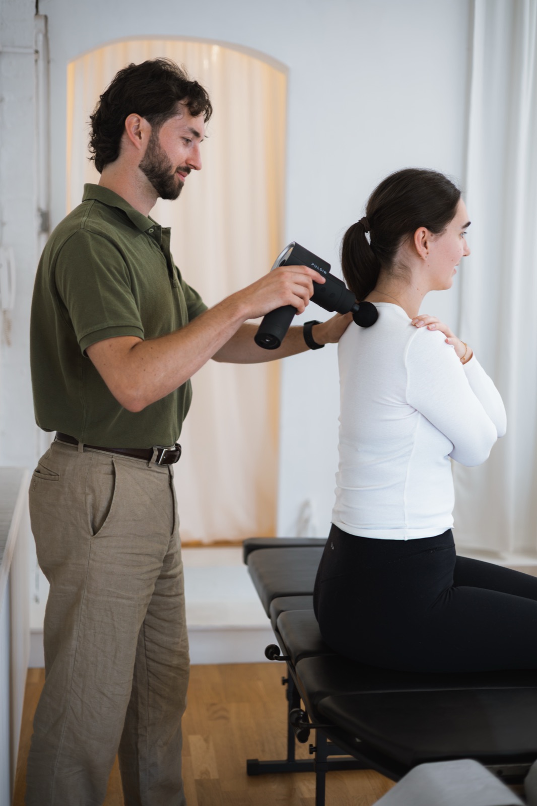Tom using a percussion massager on a patient's neck and shoulders